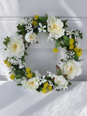 Konstgjord krans med blommor i vitt och gult. Besök Blickfång.se